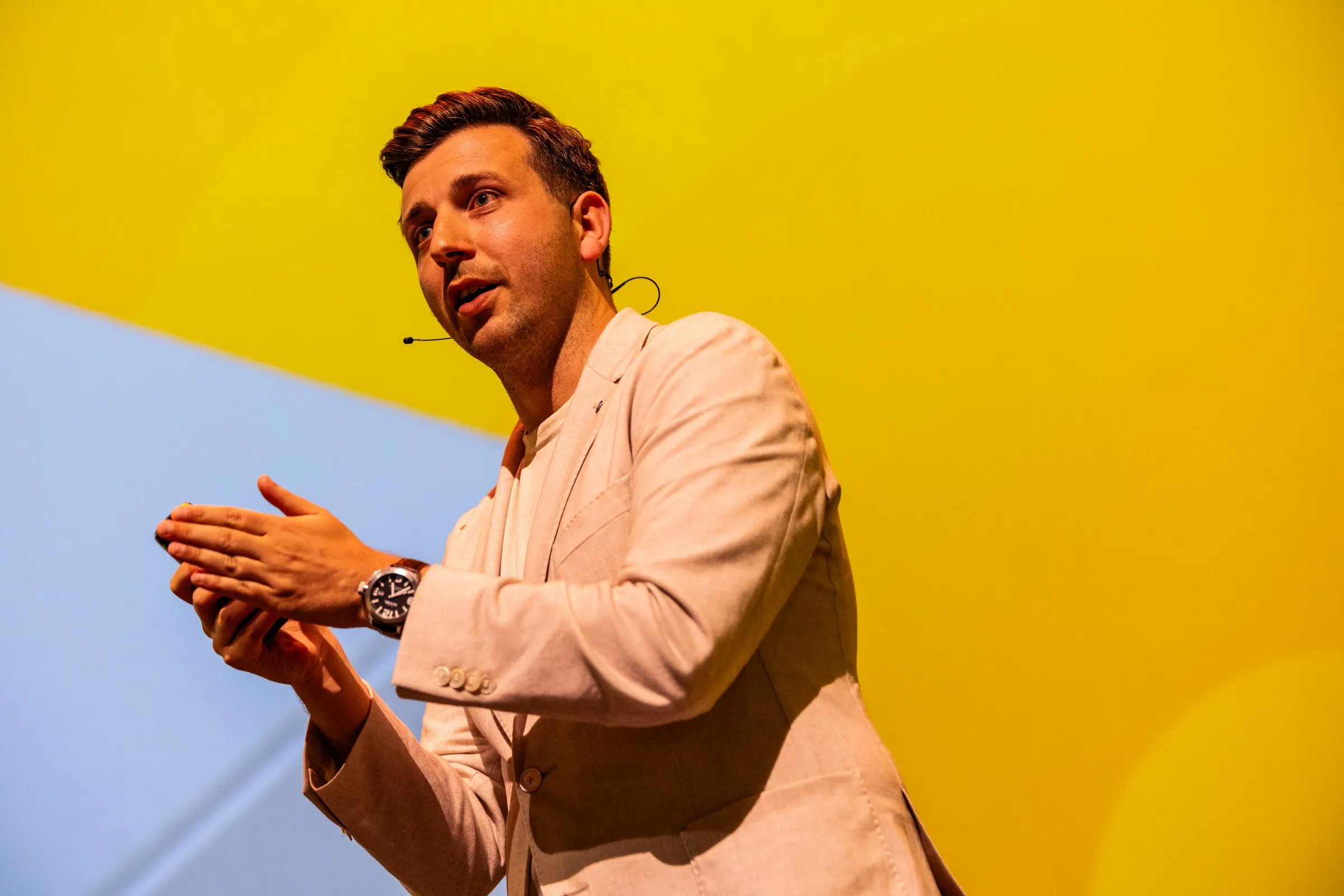 Milan van der Meulen spreekt op het podium met geel en blauw decor.